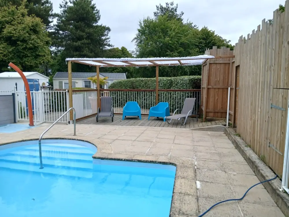 Piscine extérieure de camping avec une terrasse surélevée équipée d'une pergola, de transats et de fauteuils bleus.
